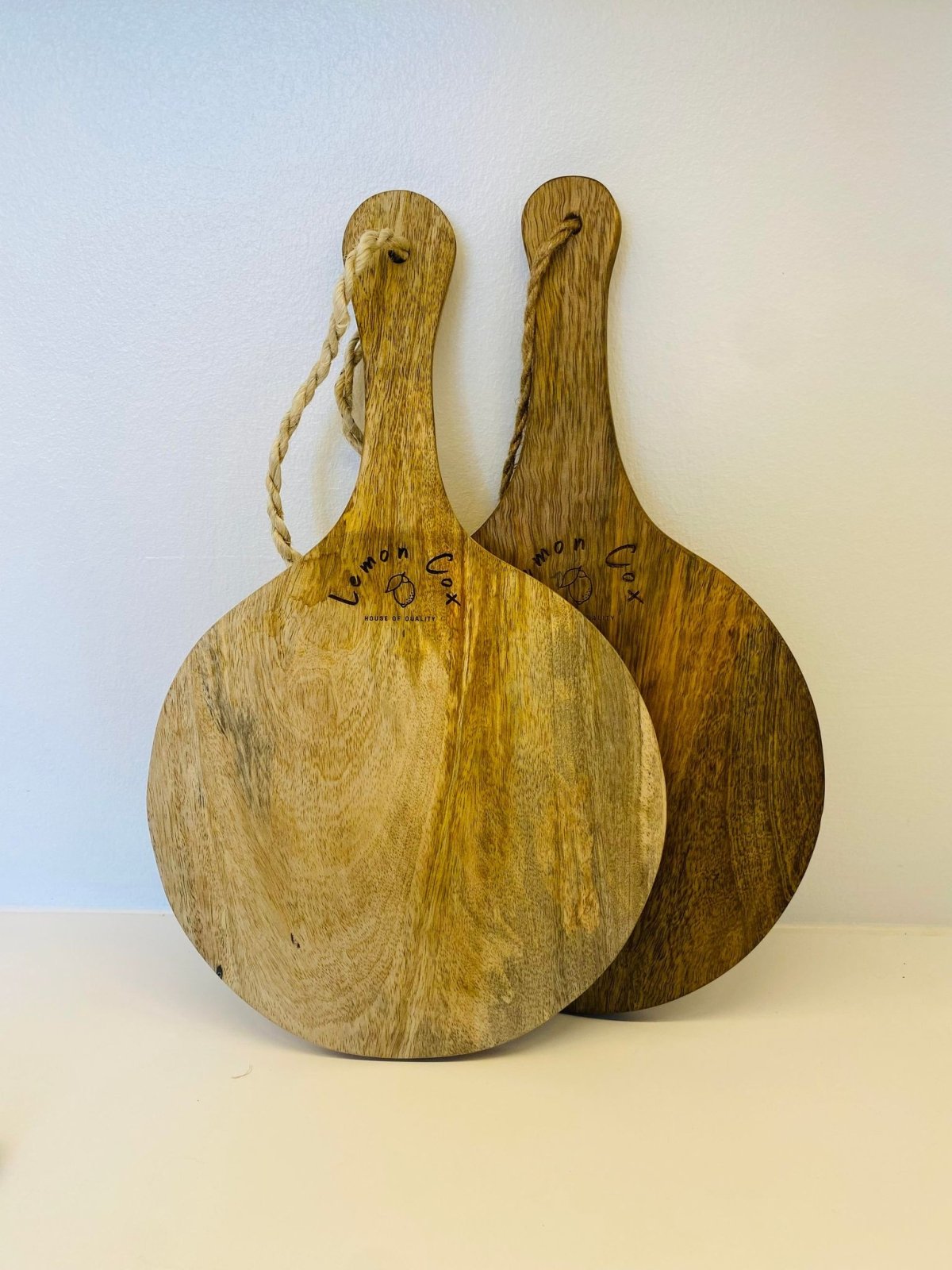 Two round Lemon Cox mango wood serving boards, branded, leaning against a wall